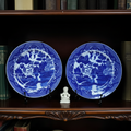 Two blue and white decorative plates on stands with a small statue in front of a bookshelf.