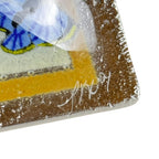 Close-up of a glass artwork with a signature, featuring blue, yellow, and brown colors.