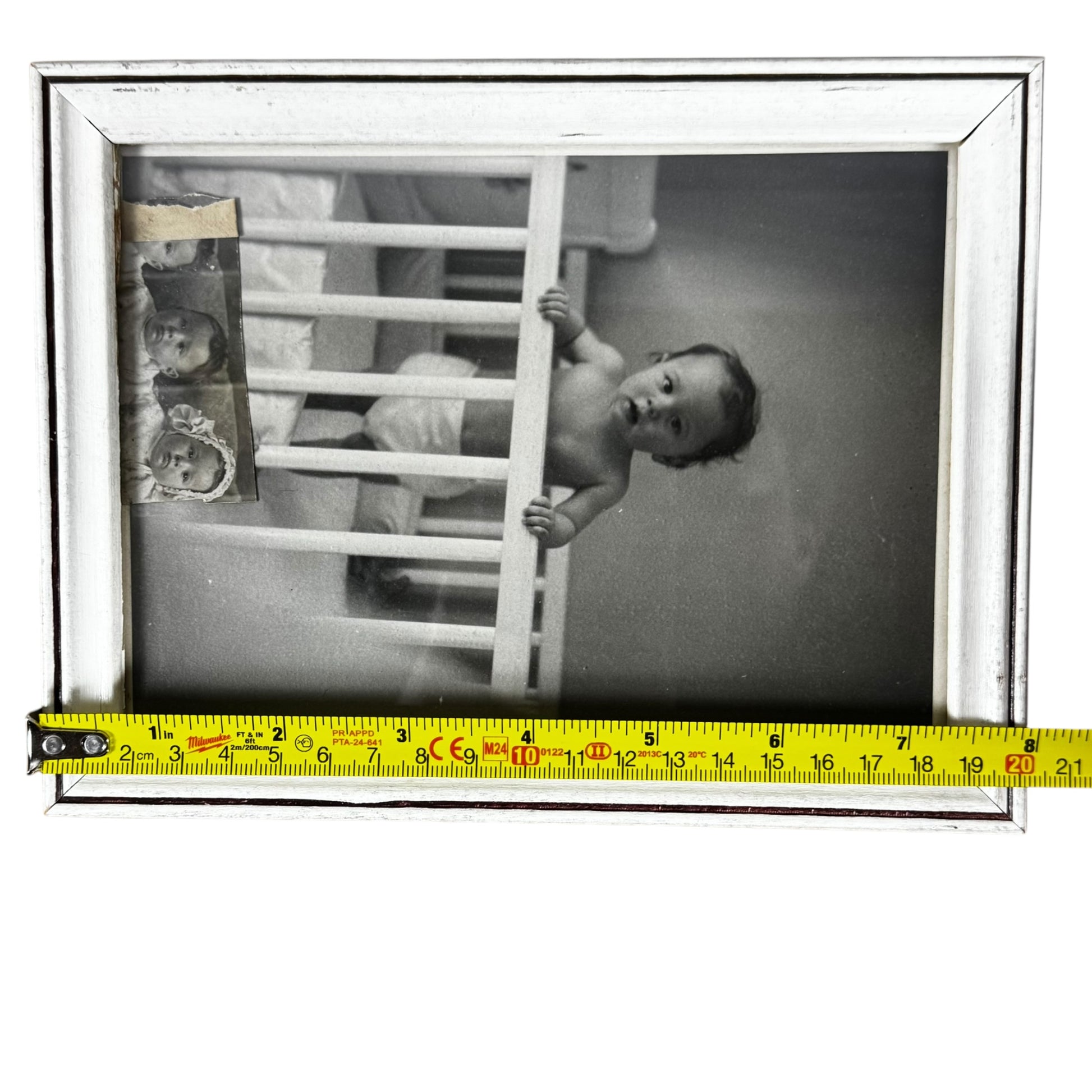 Black and white photo of a baby in a crib with a measuring tape at the bottom.