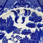 Close-up of blue and white ceramic pattern with birds, trees, and buildings.