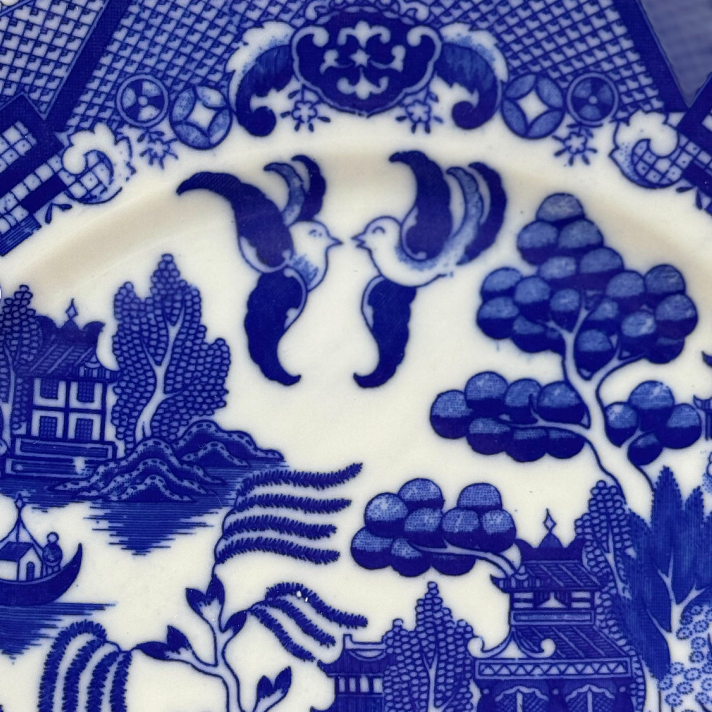 Close-up of blue and white ceramic pattern with birds, trees, and buildings.